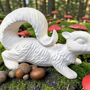 May include: A matte white ceramic squirrel figurine featuring a textured fur pattern and a large, curved tail. The squirrel is positioned in a horizontal, alert stance with its head turned slightly to the right, showcasing detailed sculpted features.