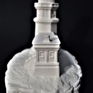 May include: White painted miniature lighthouse figurine with a detailed design, featuring a tower with a small roof and a base that resembles a rocky cliff.