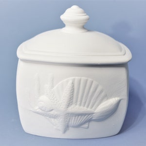 May include: White ceramic box with a lid and a raised design of a starfish and seashell. The box is perfect for storing small items.