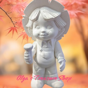 Könnte beinhalten: Eine weiße Keramikfigur eines Kindes mit Hut und Latzhose, das einen zylindrischen Gegenstand hält. Die Figur hat rosige Wangen und einen lächelnden Ausdruck. Der Hintergrund ist eine verschwommene Herbstszene mit roten Blättern und dem Text "Olga's Treasure Shop".