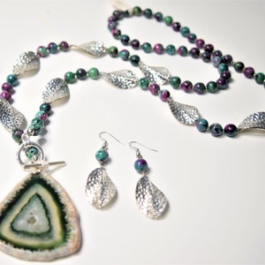 May include: A green and pink gemstone necklace with silver leaf accents and a matching pair of earrings. The necklace features a large, triangular pendant with a green and white agate slice.