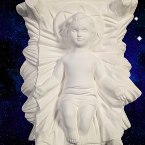 May include: White ceramic figurine of a baby Jesus lying in a manger. The figurine is detailed with a halo and a star above the baby's head.