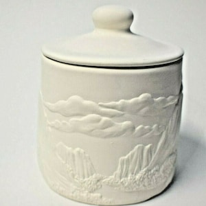 May include: White ceramic jar with a lid, featuring an embossed design of clouds and mountains. The jar is perfect for storing small items like jewelry, trinkets, or bath salts.