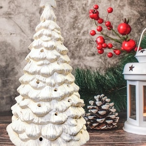May include: A white ceramic Christmas tree figurine with a textured, layered branch design and small circular cutouts throughout. The tree is topped with a single star and sits on a cylindrical base, featuring a matte finish and a conical shape.