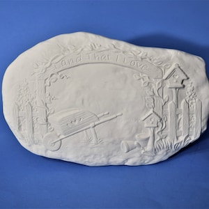 May include: White ceramic plaque with a raised design of a wheelbarrow, birdhouses, and a fence. The plaque has the text "Land That I Love" written on it.