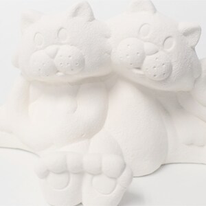 May include: White ceramic figurine of two cats sitting together. The cats are facing forward with their heads touching. The figurine is unpainted and ready to be decorated.
