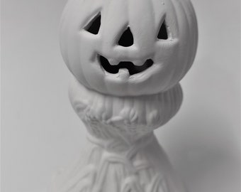 May include: White ceramic pumpkin with a carved jack-o'-lantern face. The pumpkin is sitting on a base that resembles a pile of hay.