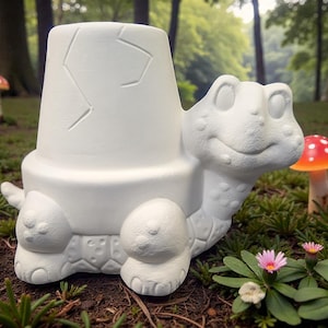 May include: A white ceramic turtle-shaped planter with a cracked eggshell design on the top. The turtle has a smiling face and detailed features. Red and orange mushroom figurines are in the background.