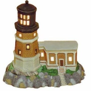 May include: A miniature ceramic lighthouse with a brown roof and brick exterior, illuminated with warm white lights. The lighthouse is set on a base with green grass and a stone path.