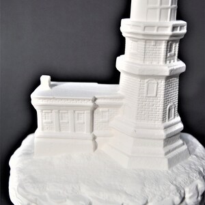 May include: White ceramic lighthouse figurine with a detailed brick exterior and a small base that resembles a rocky cliff.