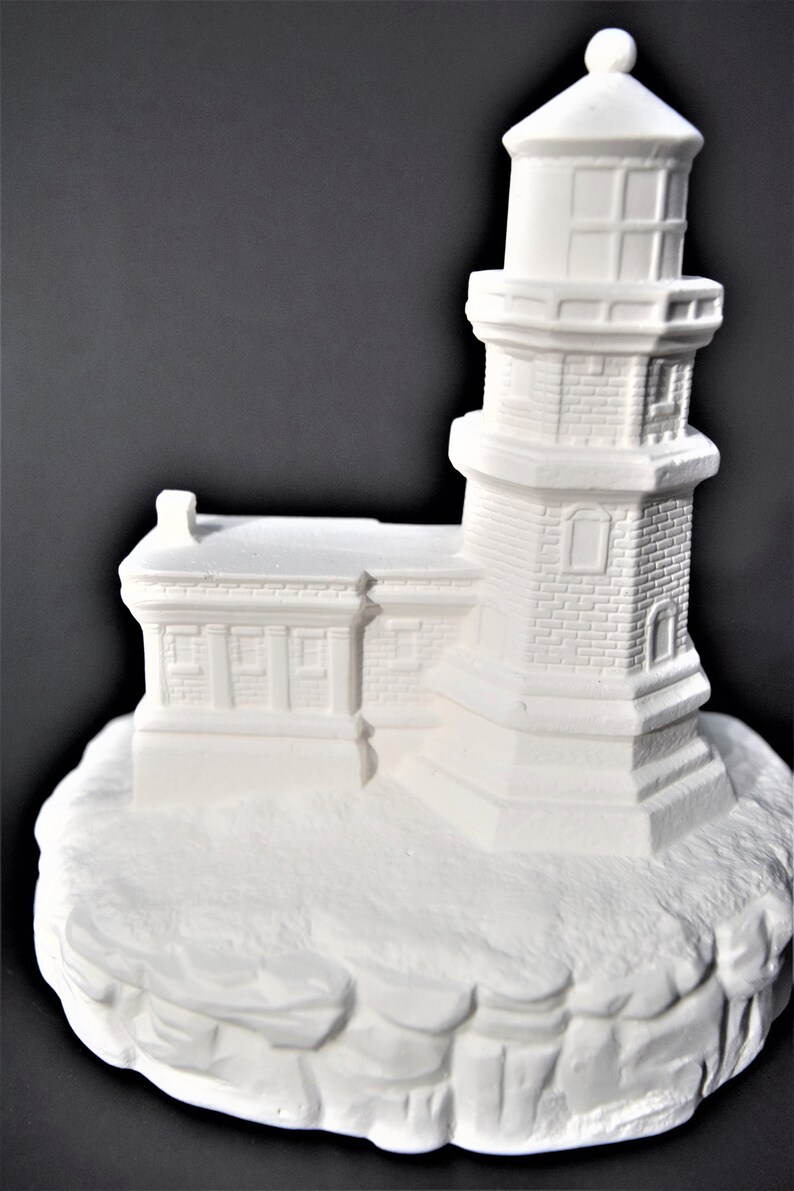 May include: White ceramic lighthouse figurine with a detailed brick exterior and a small base that resembles a rocky cliff.
