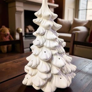 May include: A white ceramic Christmas tree with a textured, layered design. The tree has a pointed top and small holes for lights. It is displayed on a dark wooden table, suggesting a festive holiday theme.