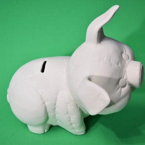 May include: White ceramic piggy bank with a textured surface and a slot on the back for coins. The piggy bank is in a side view position with its head turned to the side.