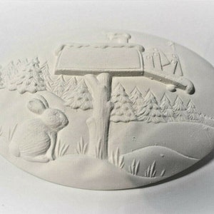 May include: White ceramic ornament with a raised design of a mailbox, a rabbit, and pine trees. The mailbox has a blank space for personalization.