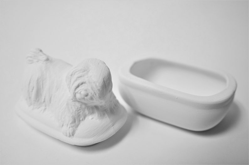 K&ouml;nnte beinhalten: Wei&szlig;e Keramik-Schmuckschatulle in Form eines liegenden Hundes. Die Schachtel ist ge&ouml;ffnet und der Deckel ist separat. Der Deckel ist in Form einer kleinen Badewanne.