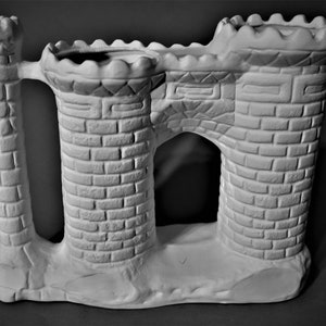 May include: White ceramic castle-shaped planter with a brick pattern and two towers. The planter has a large opening in the center.