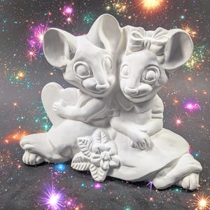 May include: A white ceramic figurine depicting two cartoon mice embracing. The mouse on the left holds a heart, while the other wears a bow. A flower is at the base of the figurine. The background is a dark space scene with colorful starbursts.