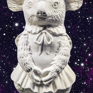 May include: A white koala bear figurine with a detailed, textured surface. The koala is wearing a ruffled collar and a bow. Its arms are crossed, and it has a skirt. The background is a purple and black galaxy.