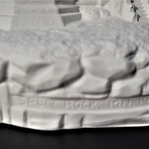 May include: White ceramic figurine of a lighthouse with a rocky base. The base is inscribed with the words "Split Rock, Jan 1910".