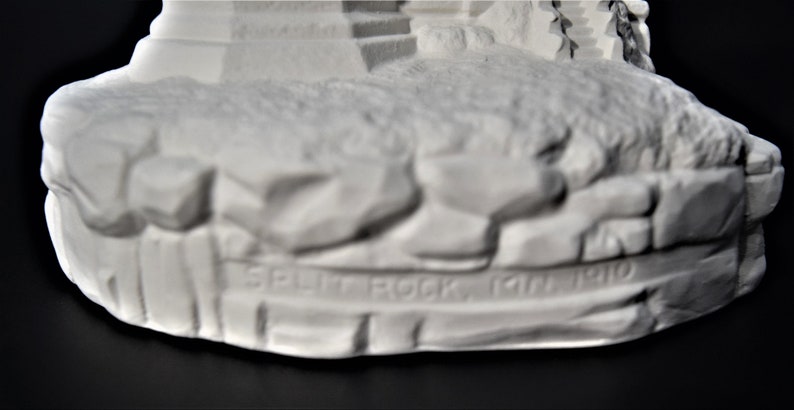 May include: White ceramic figurine of a lighthouse with a rocky base. The base is inscribed with the words "Split Rock, Jan 1910".