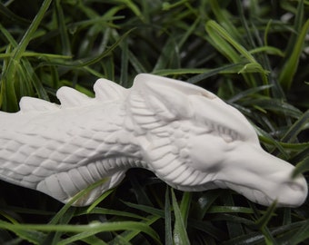 May include: White ceramic dragon head figurine with detailed scales and a textured surface. The figurine is lying on a bed of green grass.