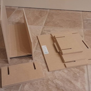 May include: Unassembled wooden shelf components. The image shows several pieces of unfinished wood, including side panels, shelves, and a base, all with slots and cutouts for assembly. The pieces are light brown and appear ready for construction.