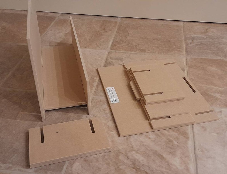 May include: Unassembled wooden shelf components. The image shows several pieces of unfinished wood, including side panels, shelves, and a base, all with slots and cutouts for assembly. The pieces are light brown and appear ready for construction.