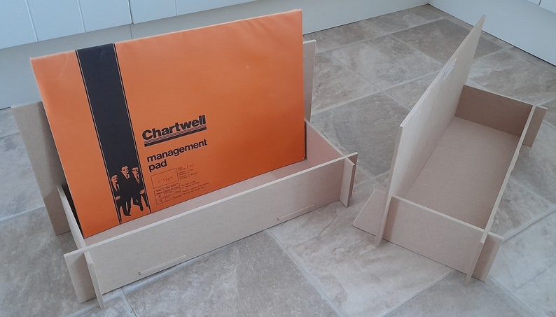 May include: An orange Chartwell management pad is displayed in a light brown wooden organizer. The organizer is made of interlocking pieces. The pad has black text and a graphic of three people in suits.