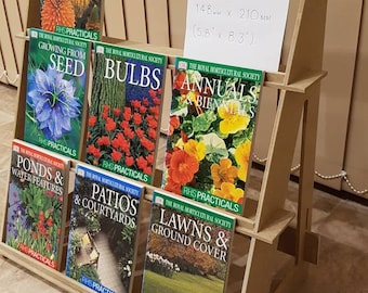 May include: A wooden display stand with a variety of gardening books. The books are titled "Hardy Perennials", "Growing from Seed", "Bulbs", "Annuals & Biennials", "Ponds & Water Features", "Patios & Courtyards", and "Lawns & Ground Cover". The stand is labeled "A5 Book Size: 148 mm x 210 mm (5.8" x 8.3")".