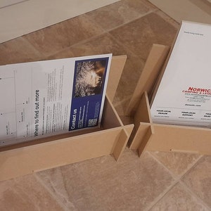 May include: Two unfinished wooden display stands, each holding printed materials. One stand displays a document with a timeline and contact information. The other features a brochure for Norwich Camping & Leisure.