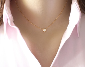 May include: A delicate gold chain necklace featuring a single, small, round, clear gemstone set in a gold bezel setting. The necklace rests against the neck, showcasing a minimalist design with a thin, polished gold link chain and a central stone.