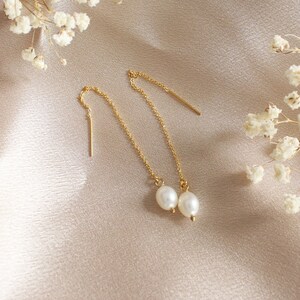 May include: A pair of gold chain earrings with a pearl dangling from each chain.