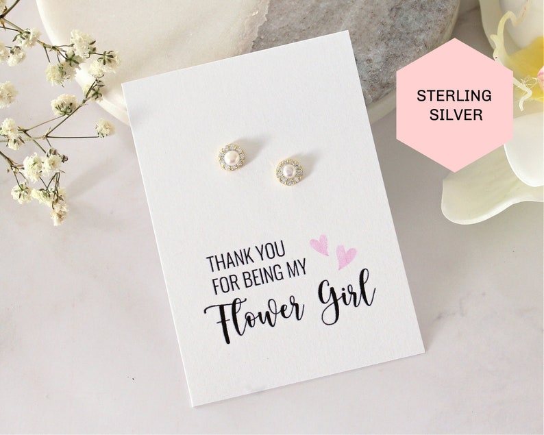 May include: A white card with the text "Thank you for being my Flower Girl" and two pink hearts. The card is next to a pair of sterling silver earrings with a pearl and clear stones.