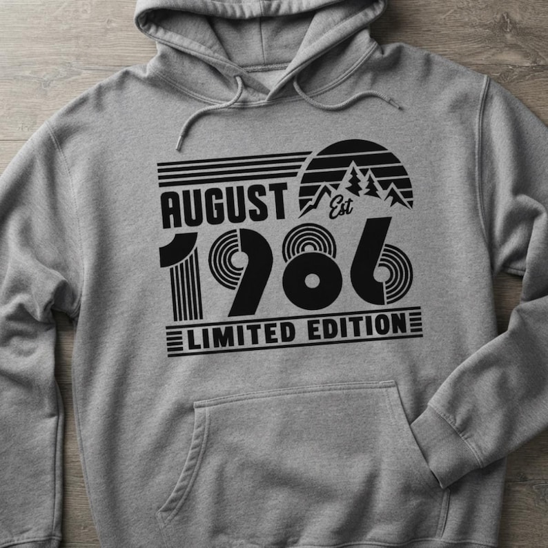 May include: A heather gray hooded sweatshirt featuring a black graphic print that reads August 1986 Limited Edition. The design includes a stylized mountain range inside a semi-circle, horizontal lines, and concentric circles within the numbers.
