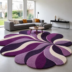 May include: A large, circular area rug featuring a stylized, multi-petaled floral design. The rug is composed of plush, textured segments in varying shades of deep purple, light violet, and cream, arranged in a swirling, radiating pattern.