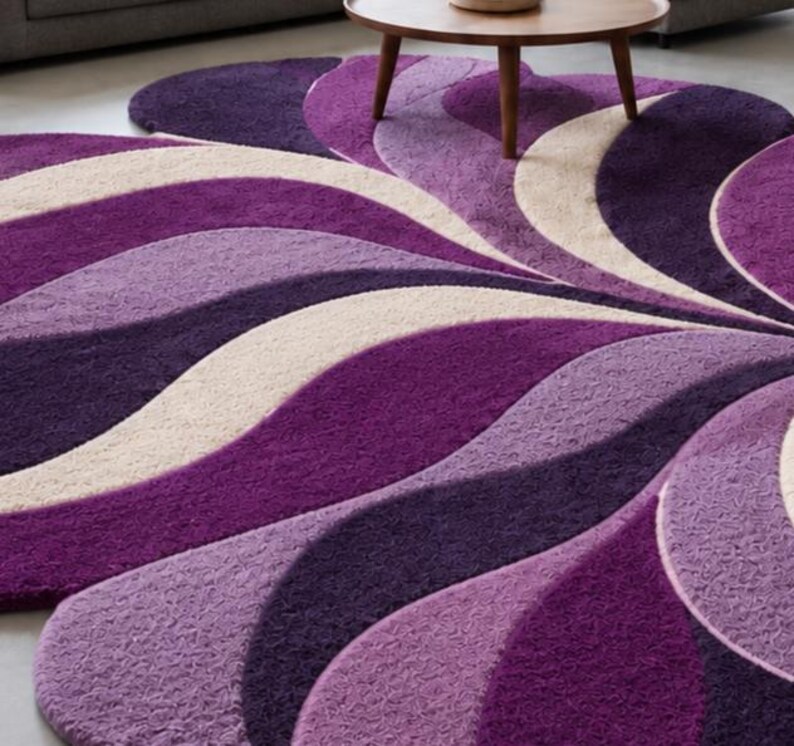 May include: A large, plush area rug featuring a repeating, wave-like pattern in shades of deep purple, lavender, and cream. The rug has a thick, textured pile and a curved, organic shape that extends across the floor, creating a layered visual effect.