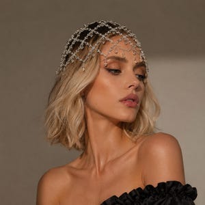 May include: A silver-toned headpiece featuring a delicate, interconnected lattice chain design. The accessory is adorned with small, clear, teardrop-shaped crystals suspended from the intersections of the metallic mesh, creating a draped effect.