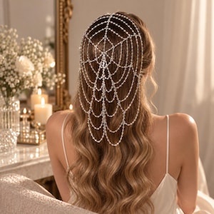 May include: A silver-toned hair accessory featuring a web-like design constructed from multiple strands of clear, sparkling crystals. The piece drapes over the back of the head, with delicate chains extending downward to create a layered effect.