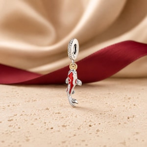 May include: A sterling silver charm bead featuring a dangling koi fish pendant with red and white enamel detailing. The bail is encrusted with small clear stones and features a small gold-toned circular accent piece above the fish figure.