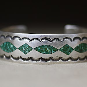 May include: A silver cuff bracelet featuring a series of alternating diamond and marquise-shaped inlays filled with small green crushed stone fragments. The metal surface is decorated with stamped scalloped patterns along the top and bottom edges.