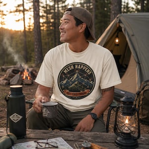 May include: A cream-coloured short-sleeve t-shirt featuring a circular graphic on the chest. The graphic depicts a mountain range overlaid with a geometric mesh network pattern, the text "MESH HAPPENS" at the top, and "OFF-GRID COMMS" on a banner.