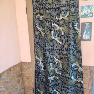 Könnte beinhalten: Ein rechteckiges Stoffpaneel mit schwarzem Hintergrund und einem sich wiederholenden Muster aus stilisierten Vögeln in Blau-, Gold- und Weißtönen, durchsetzt mit floralen Motiven. Das Textil zeigt durchgehend ein komplexes Linienmuster.