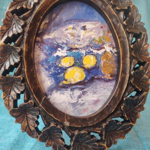 Può includere: Una cornice ovale in legno con un bordo intagliato a foglie che racchiude un dipinto a olio. L'opera raffigura tre limoni giallo brillante appoggiati su una superficie blu e bianca testurizzata con pennellate spesse e visibili.