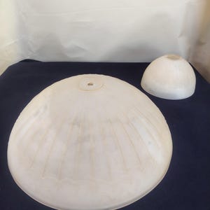 May include: Two off-white, translucent glass lamp shades with a ribbed, shell-like pattern. The larger shade is a wide, shallow dome with a central hole, while the smaller shade is a compact, rounded dome shape with a smooth, circular opening.