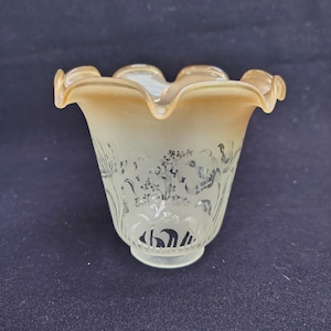 Op de afbeelding: Een lampenkap van matglas met een gegolfde, amberkleurige rand. De behuizing heeft een doorschijnende witte afwerking, versierd met een geëtst, zilverkleurig bloemmotief van bladeren en bloesems rondom het onderste deel van de klokvorm.