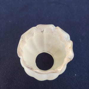 May include: A cream-colored glass lamp shade featuring a fluted, scalloped edge design. The shade has a circular opening at the top and a wider, ruffled opening at the bottom, with a smooth, matte finish throughout the exterior surface.