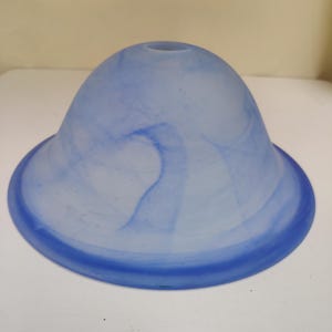 Op de afbeelding: Een koepelvormige glazen lampenkap met een matte afwerking en wervelende patronen in licht- en donkerblauw. De kap heeft een ronde opening aan de bovenkant en een bredere, gladde ronde opening aan de onderkant met een gemarmerd effect.