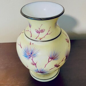 May include: A yellow glass vase with a white interior and a silver rim. The vase is decorated with a floral pattern in shades of purple and blue.
