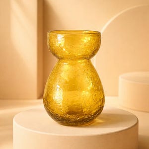 May include: A yellow glass vase with a crackle finish. The vase has a bulbous base and a narrower neck, sitting on a round, off-white pedestal. The background is a soft, neutral tone.