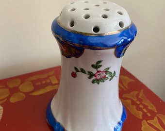 May include: White ceramic flower frog with blue and gold trim and floral designs. The frog has a round top with holes for holding flowers.